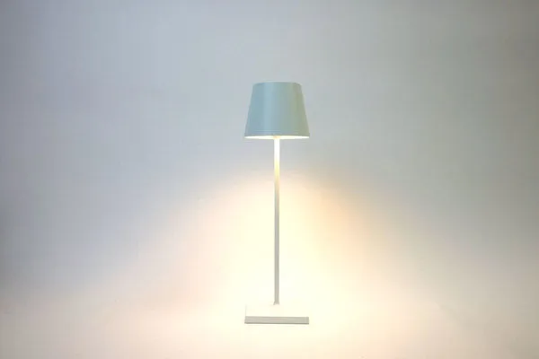 White modern table lamp with a slim metal frame and a tapered shade emitting soft white light